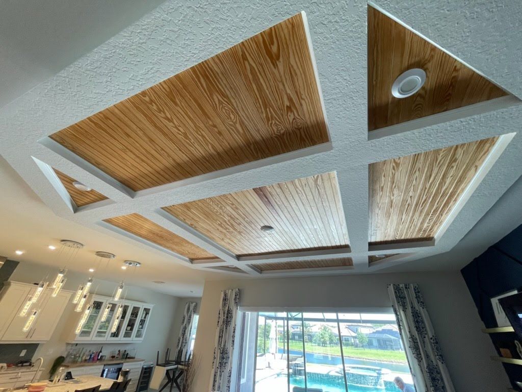 Wooden paneled ceiling with recessed lighting, framed by textured white material, over a living space.