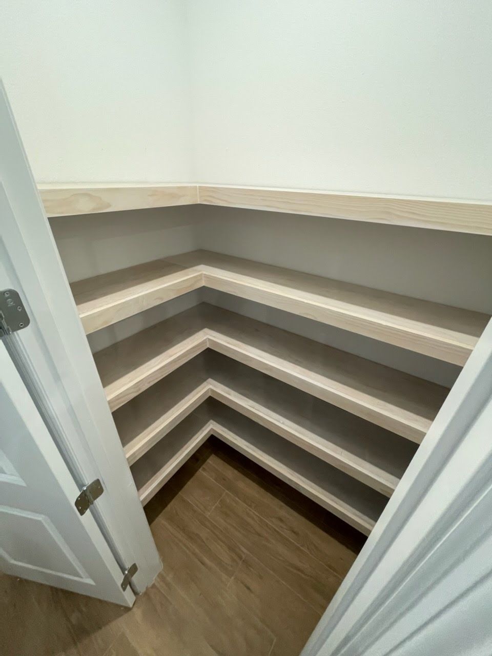 A pantry with multiple shelves, white walls, and a wooden floor, viewed from the doorway.