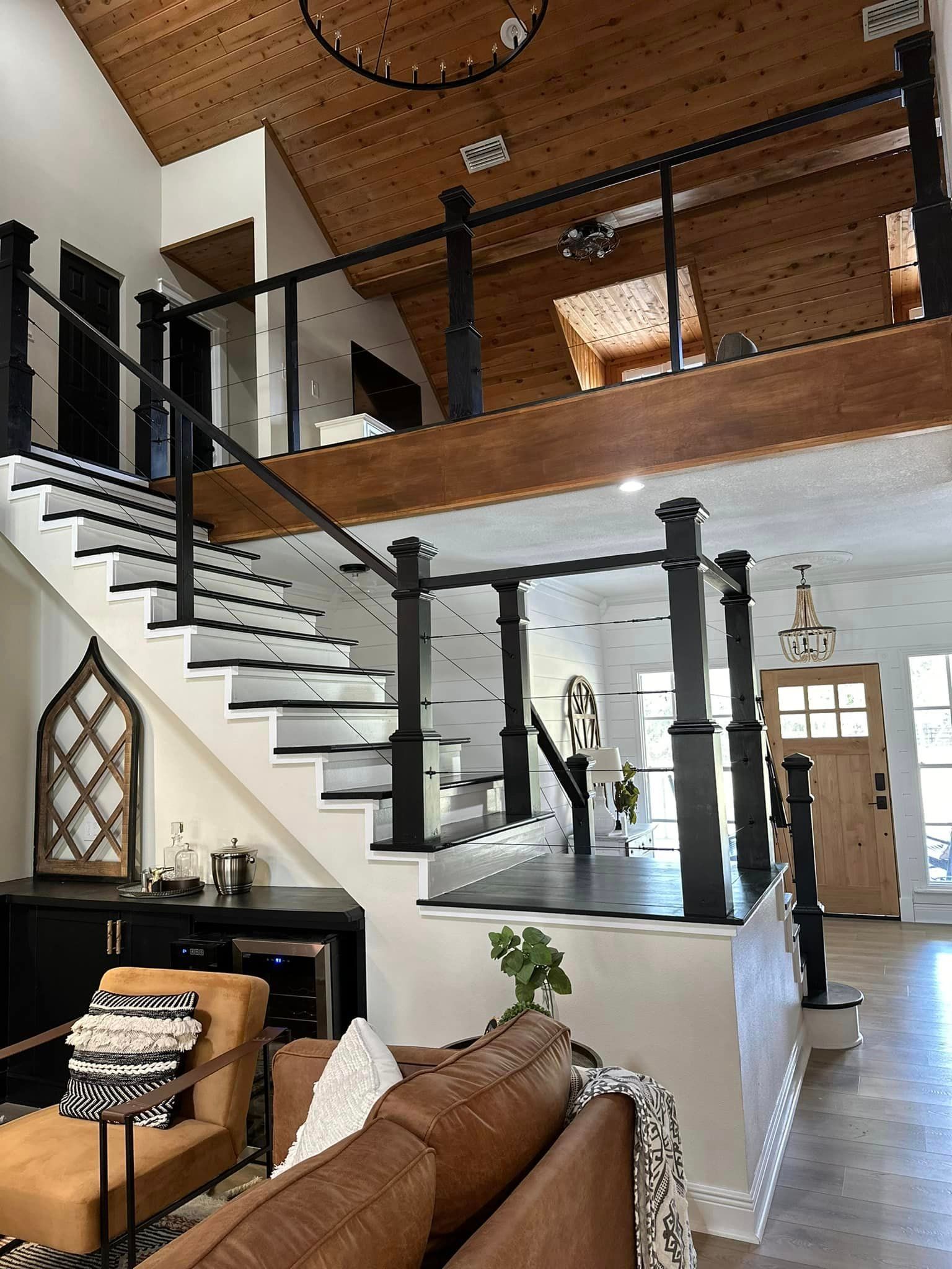 Staircase with black and white steps and railing. Interior with wood ceiling and floors. Leather sofa and armchair.