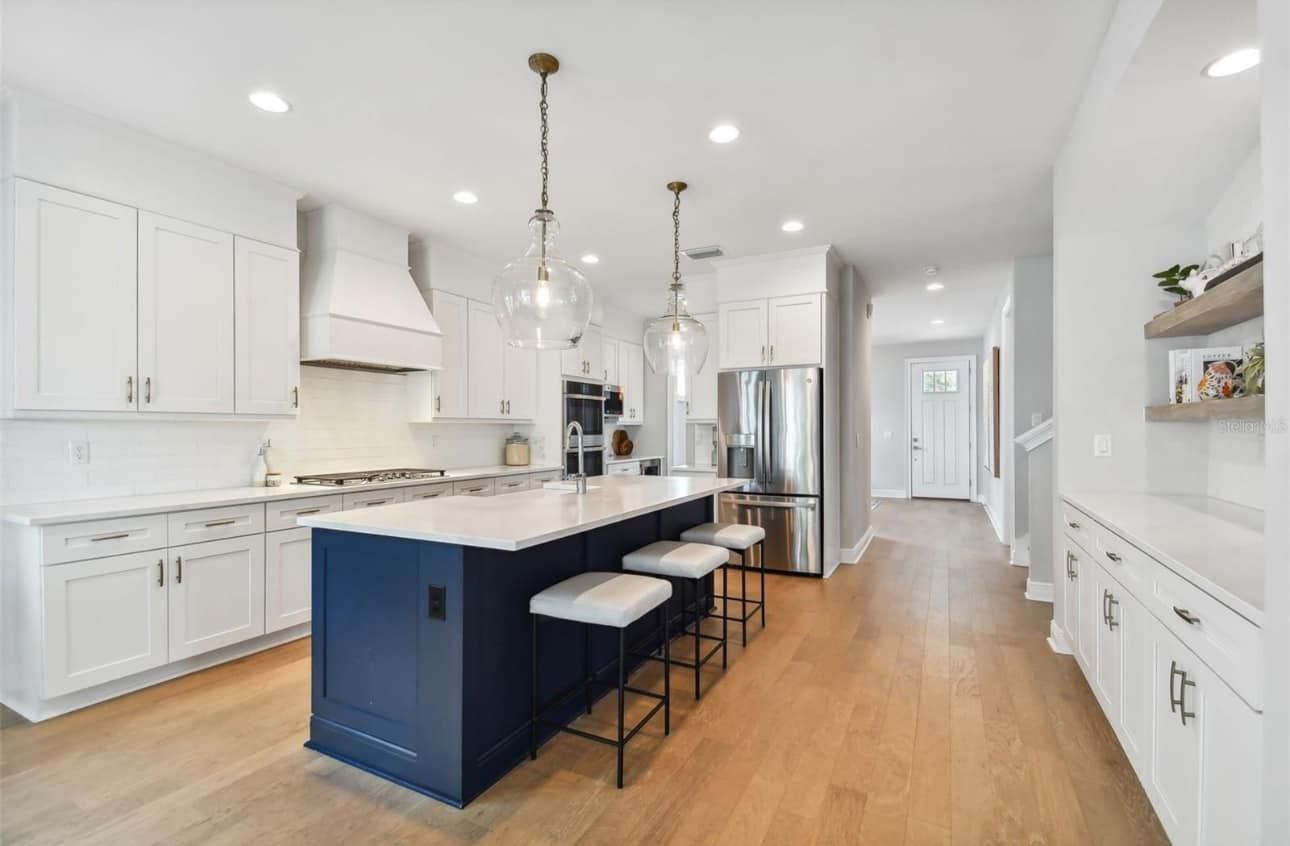 Modern white kitchen with navy island, pendant lights, and hardwood floors.