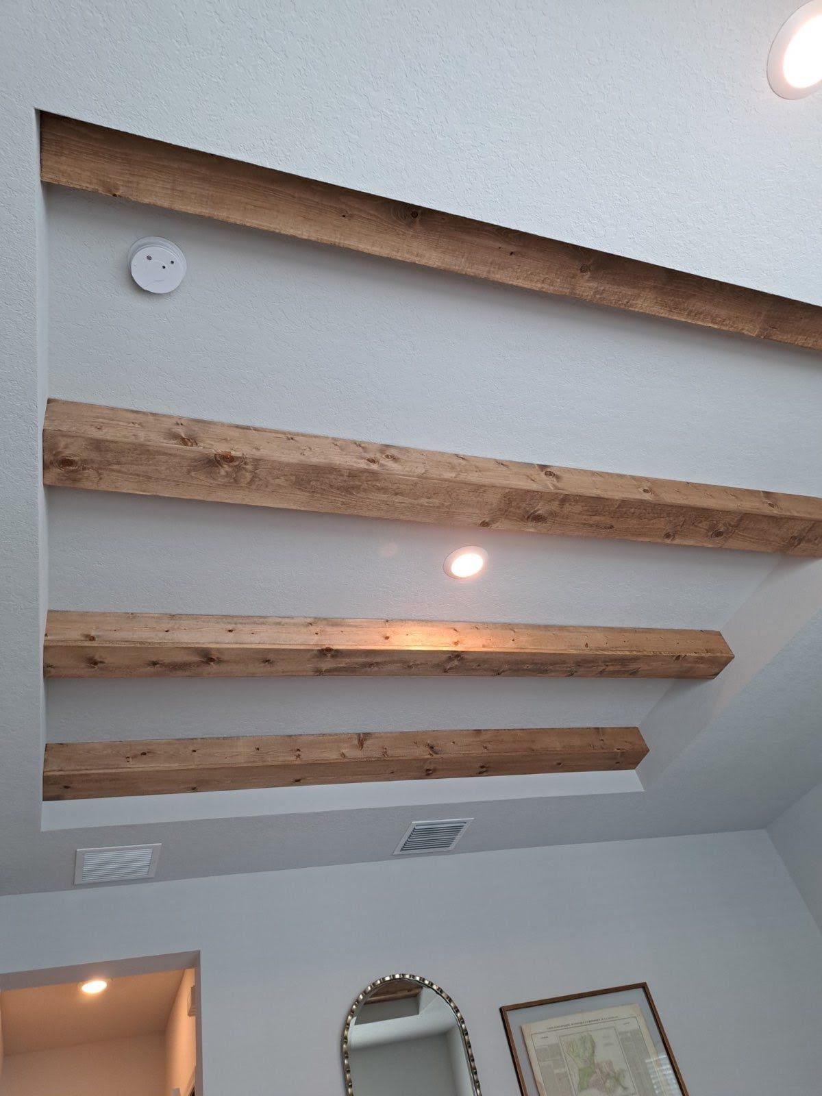 Ceiling with recessed panel and wooden beams. Beige walls. A smoke detector and lights are present.