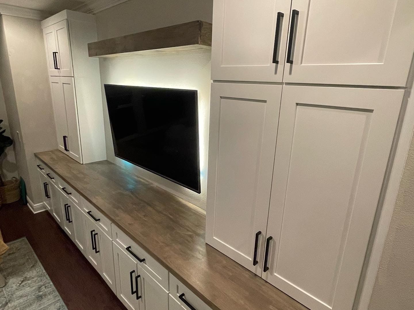 Built-in white cabinets and media center with a TV, wooden countertop, and black hardware.