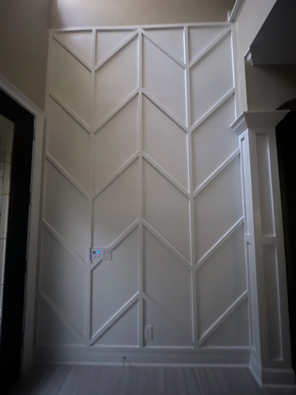 White wall with chevron pattern molding. Light switch and electrical outlet visible.