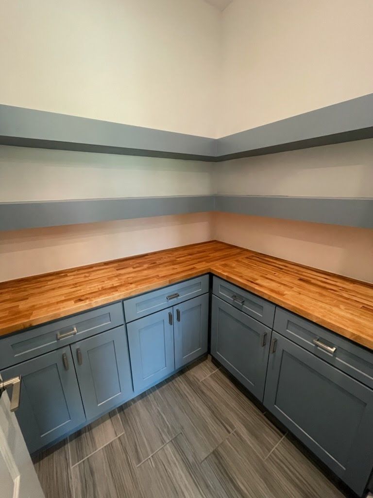 Blue cabinets with wood countertop in a pantry, with gray and blue striped walls and tile floor.
