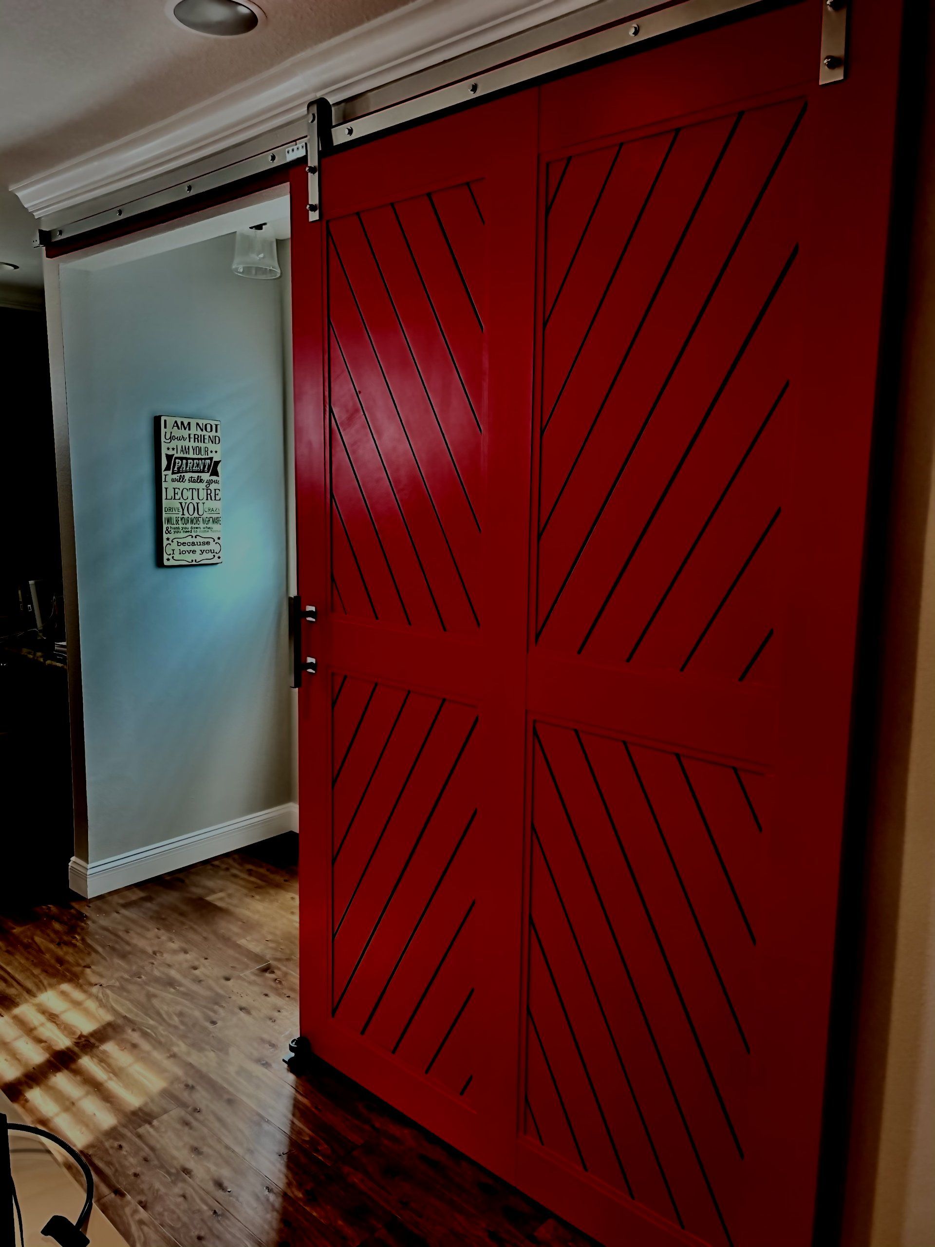 Red barn door with black diagonal accents, on a sliding track, in a hallway.