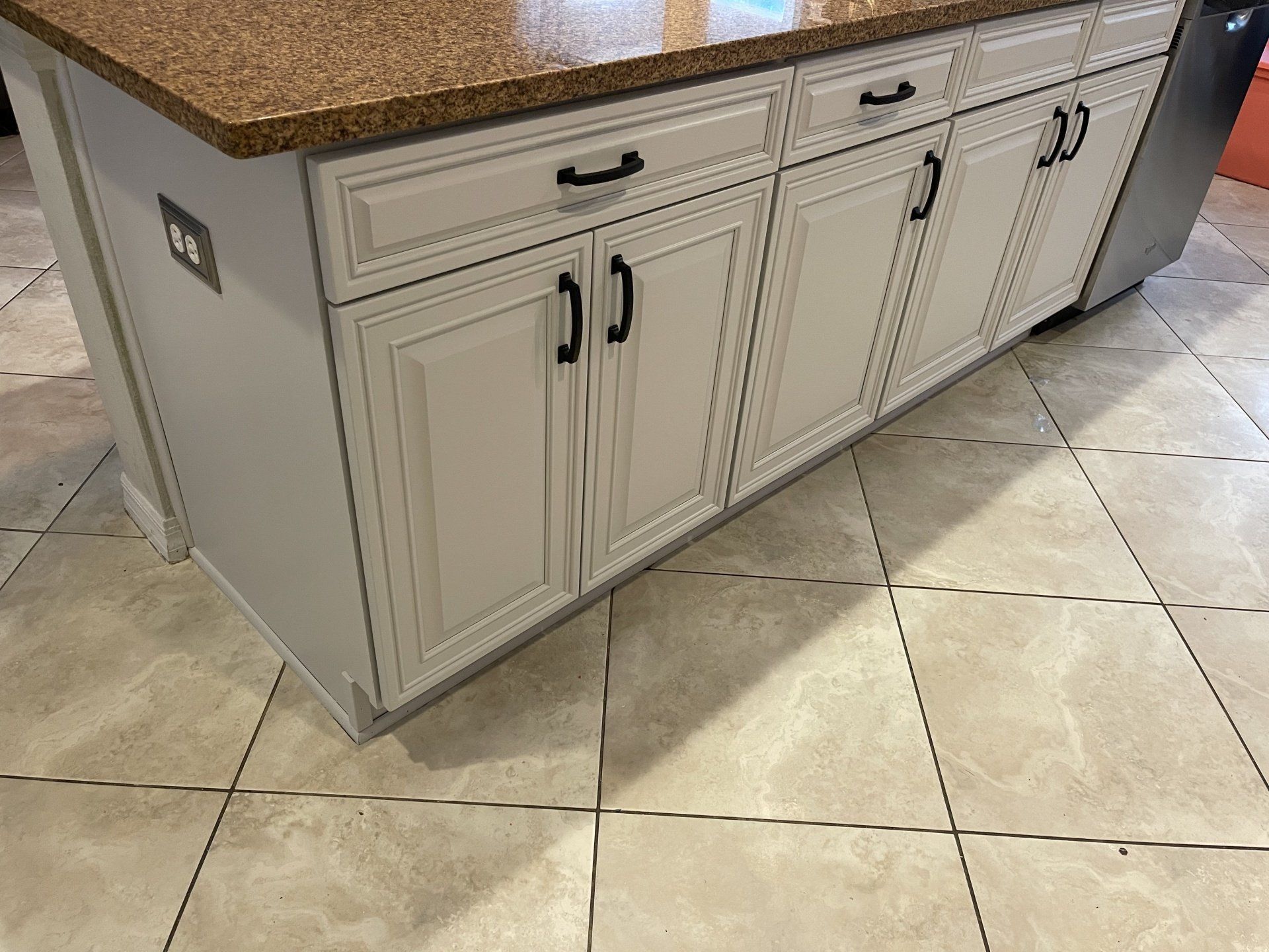 Kitchen island with white cabinets, black hardware, and a brown countertop.