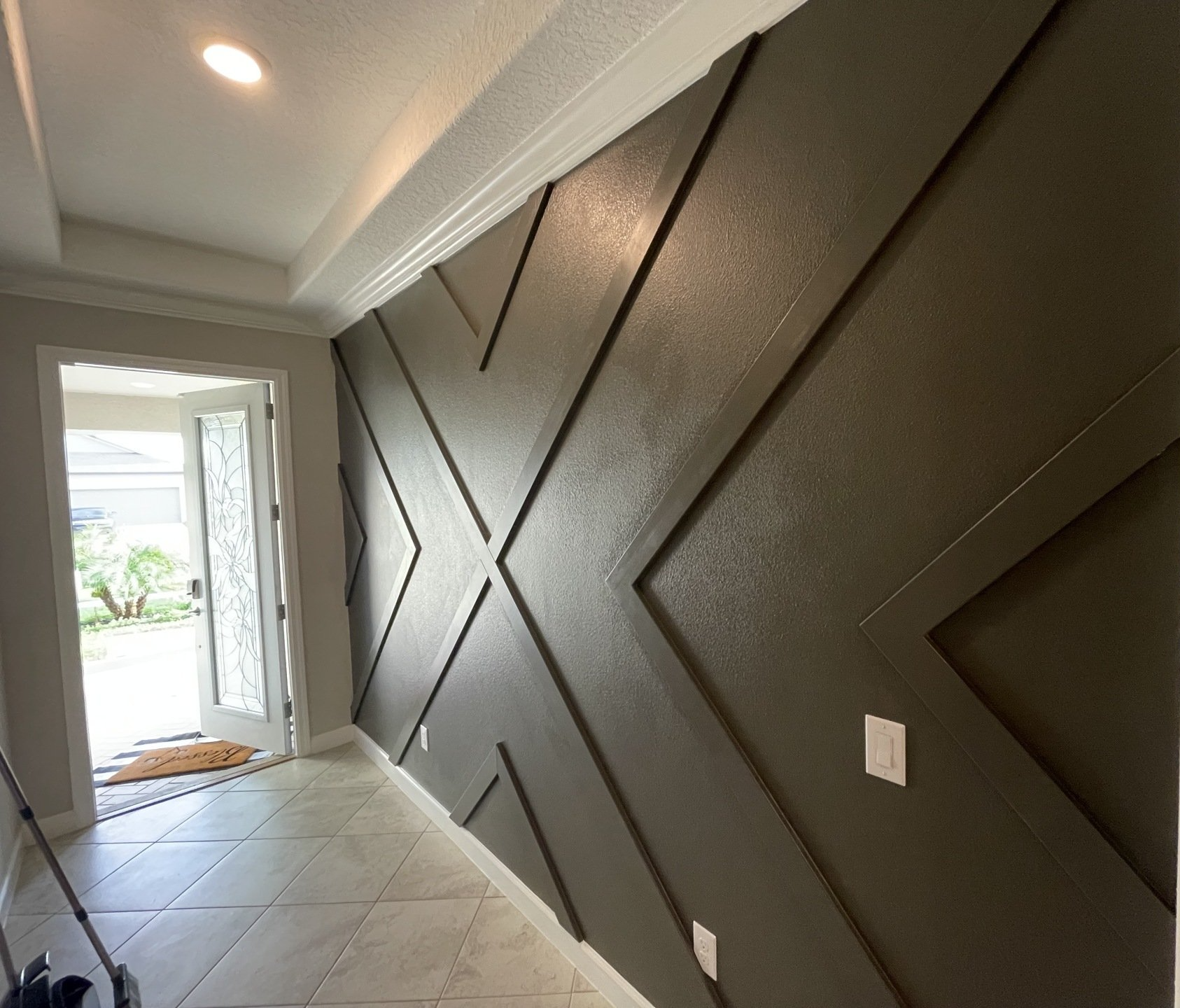 Dark accent wall with geometric wood trim, next to a doorway and a light switch.