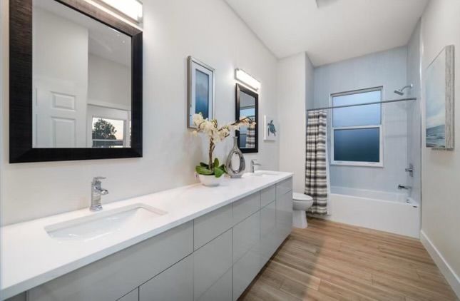 Modern bathroom with white vanity, sinks, mirrors, and a shower/tub combo.