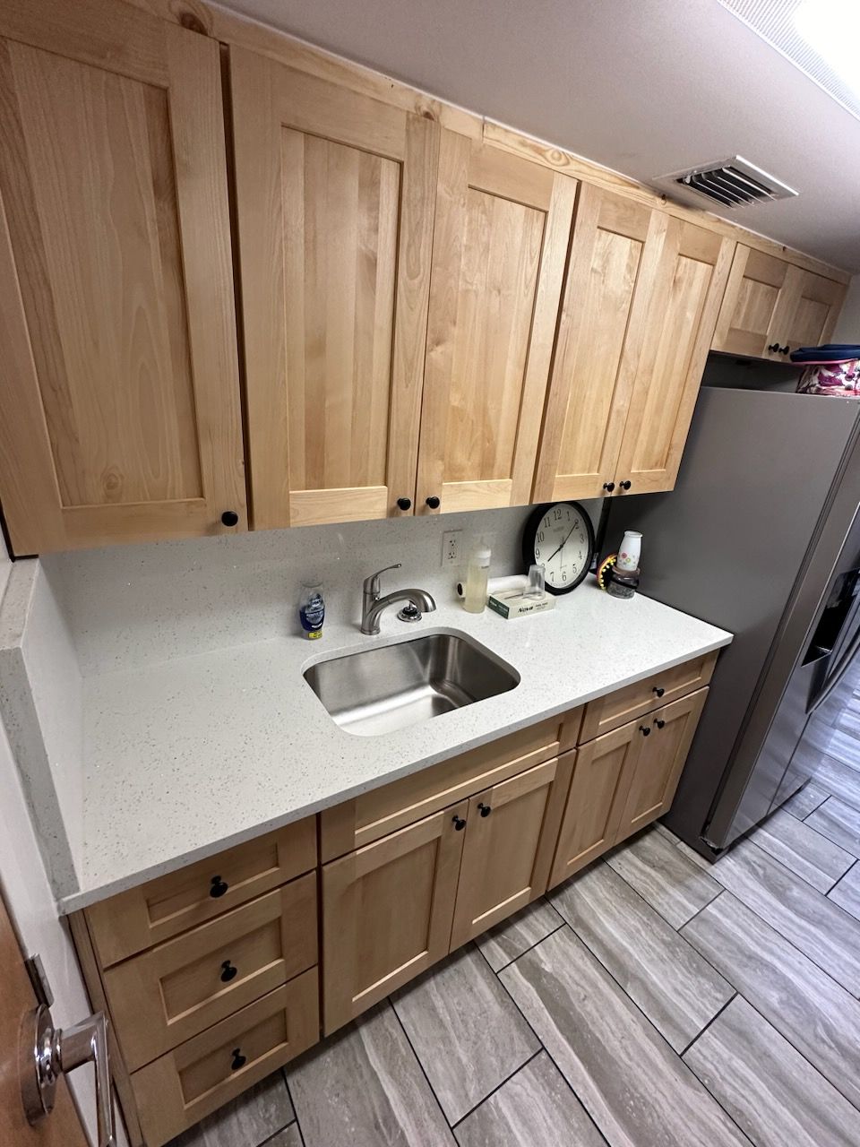 Kitchen with light wood cabinets, stainless steel sink, and gray countertop and flooring.