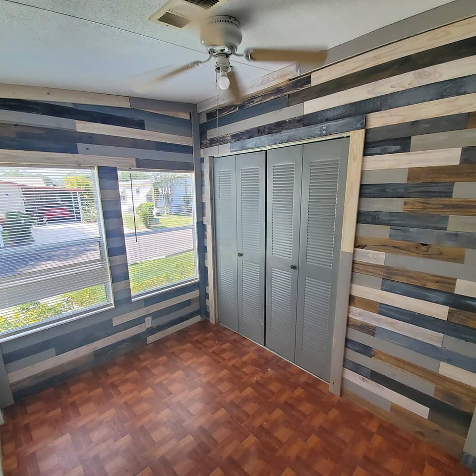 Small room with wood plank walls, closed grey closet, and two windows overlooking a street.