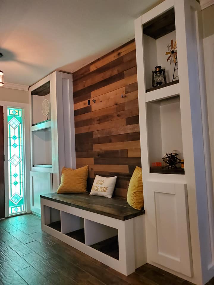 Built-in entryway bench with storage, wood accent wall, white shelving, and decorative pillows.