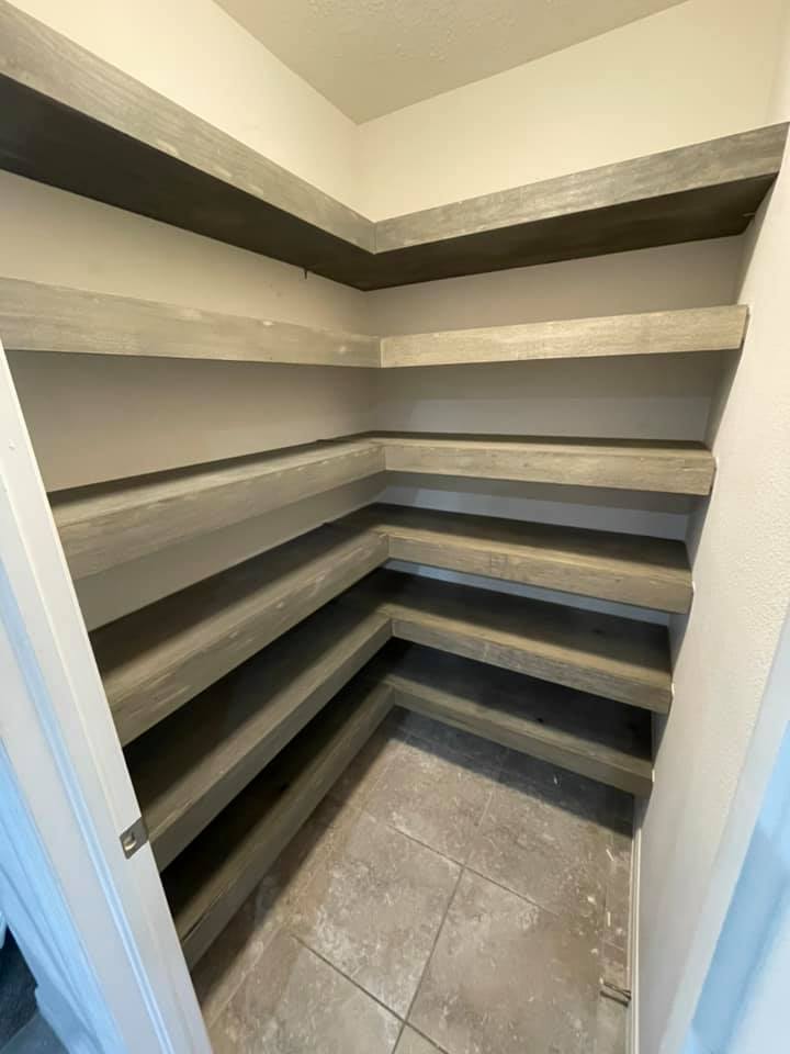 Built-in pantry with light gray shelves in a corner. Off-white walls, tile floor.