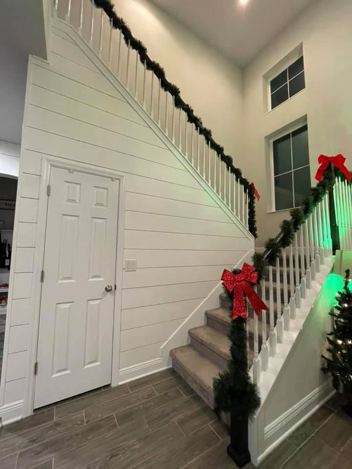 Staircase decorated for Christmas: garland with red bows, on white paneling. Door on the left.