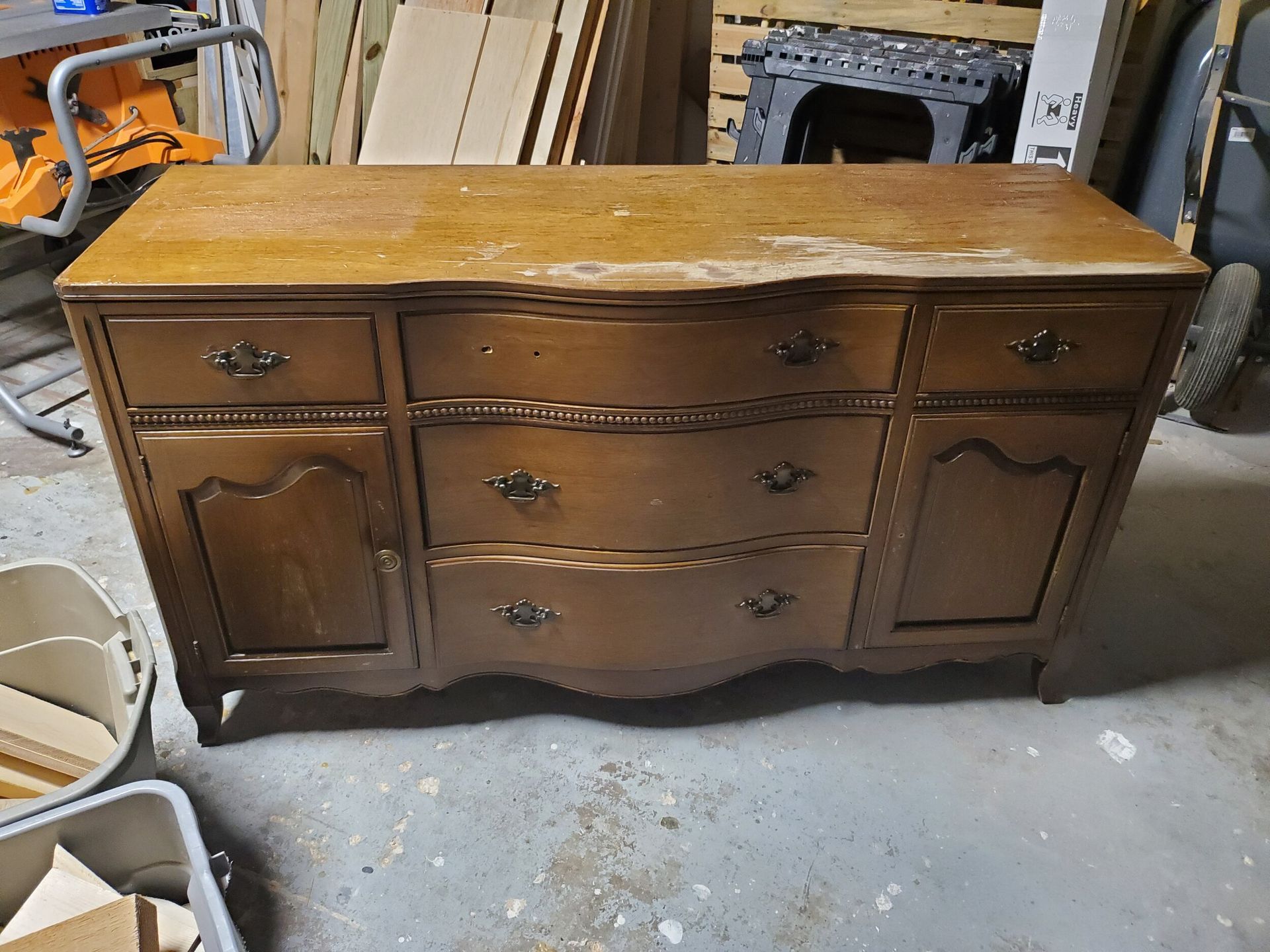 Wooden buffet cabinet with drawers and doors in a cluttered workshop.