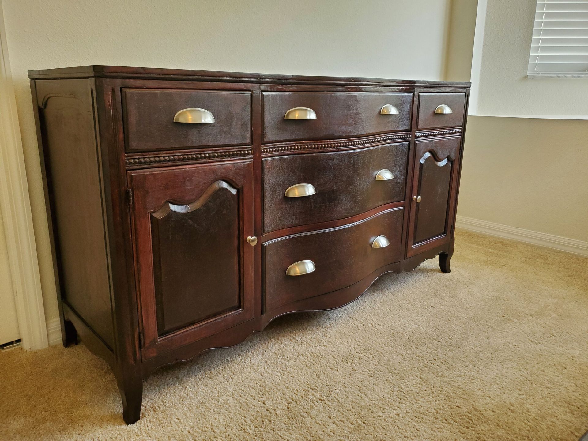 Dark brown antique dresser with silver handles on beige carpet.