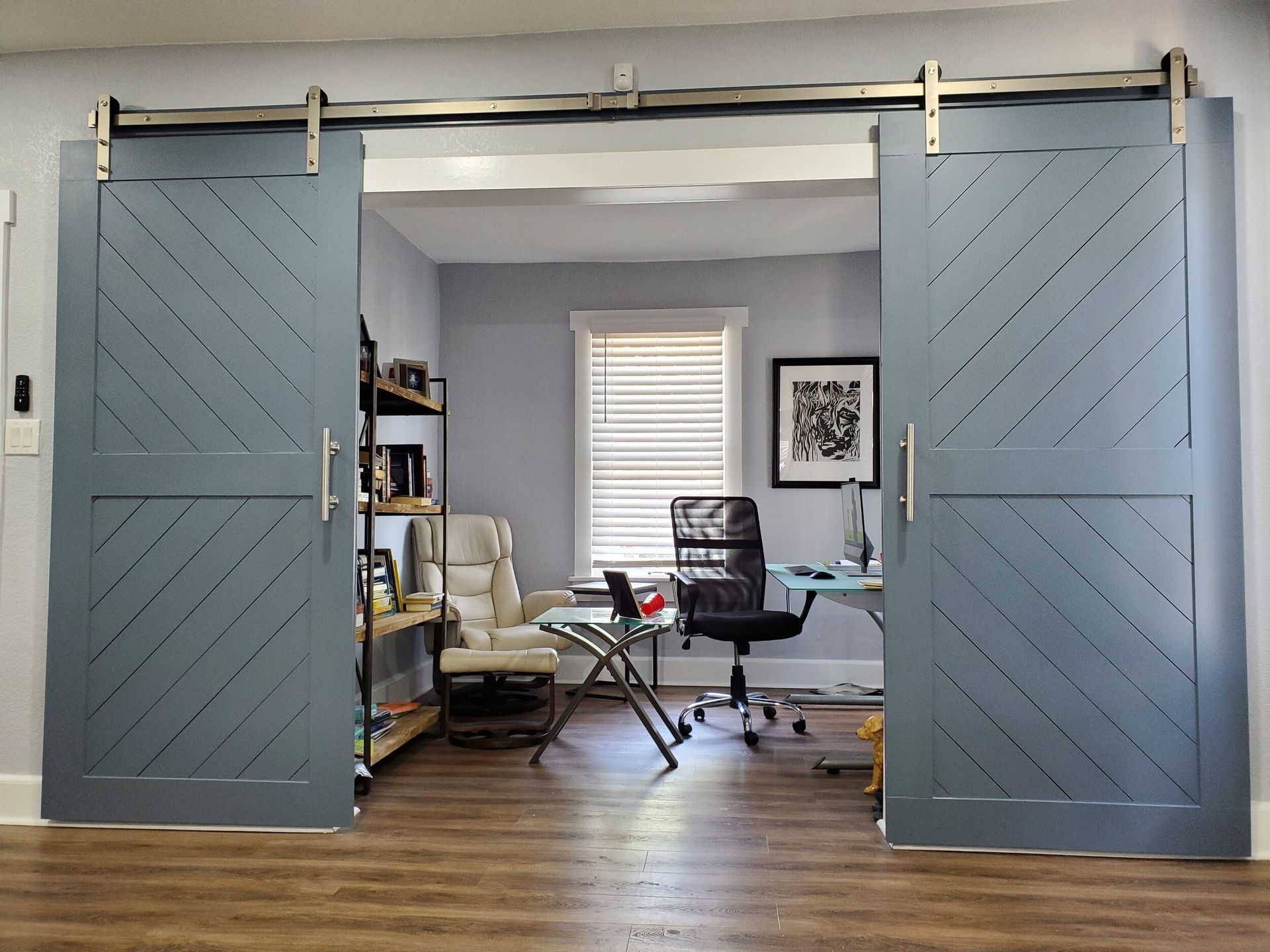 Blue sliding barn doors open to an office with desk, chair, shelves, and window.