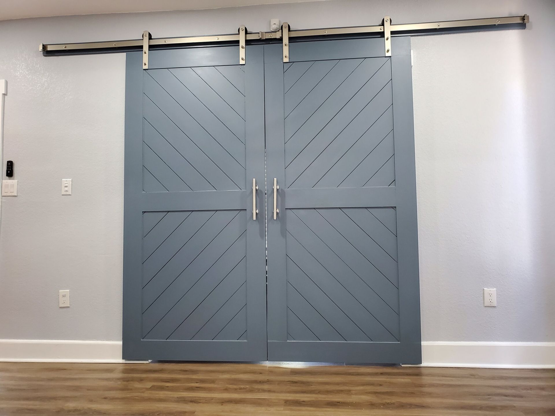 Blue barn doors with a diagonal pattern, hanging on a metal track.
