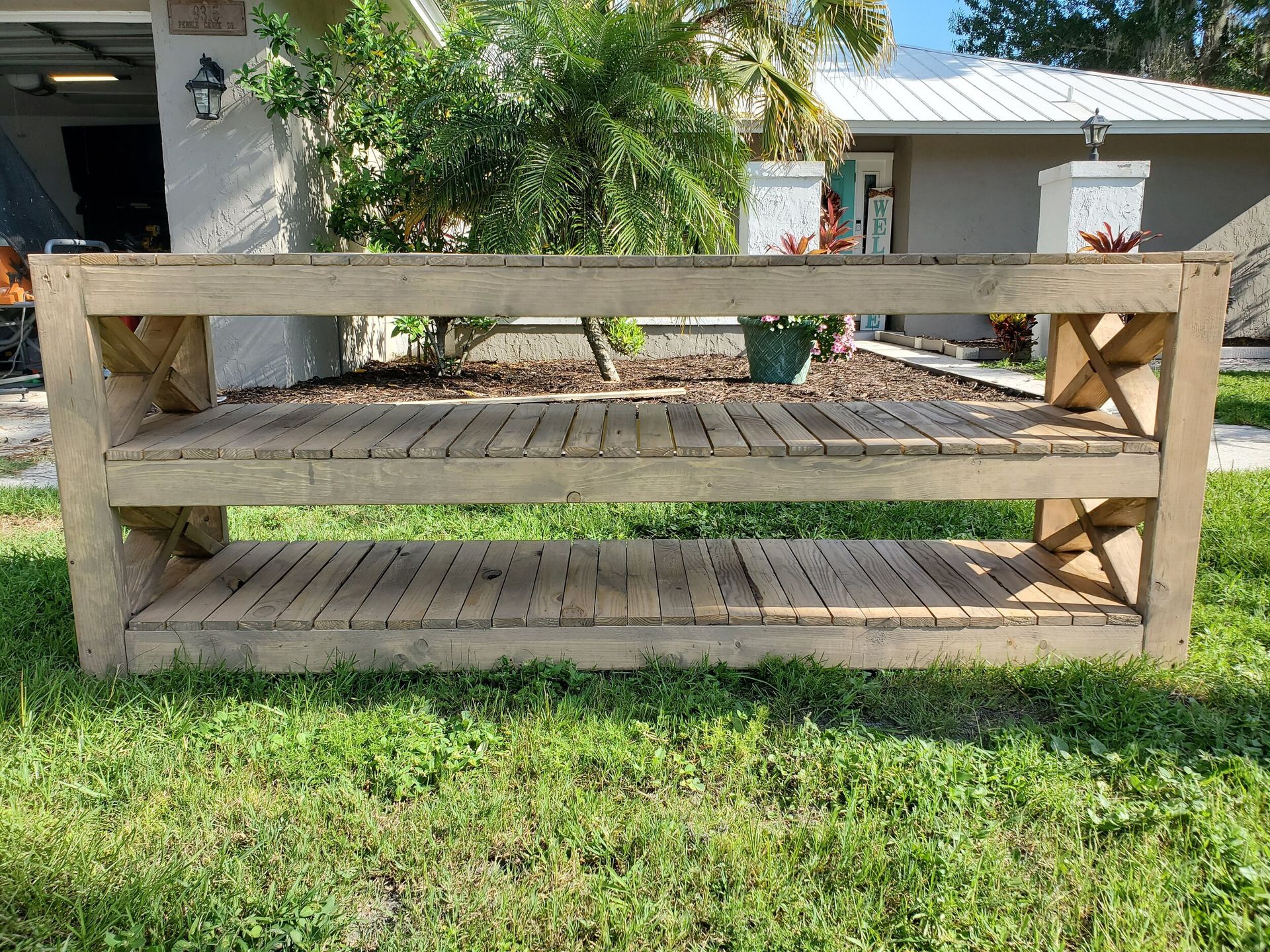 Wooden outdoor console table with two shelves, on a grassy lawn.