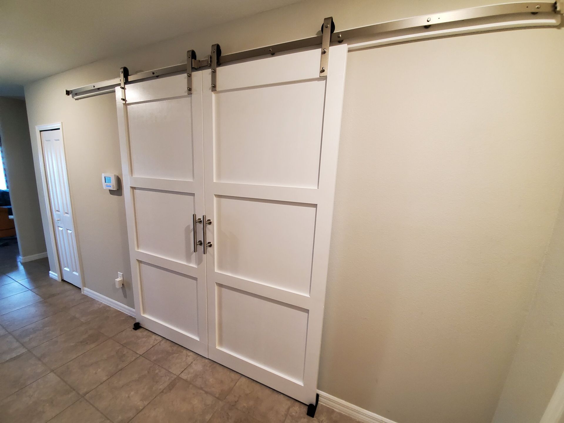 White sliding barn doors with black hardware on a light beige wall and tiled floor.