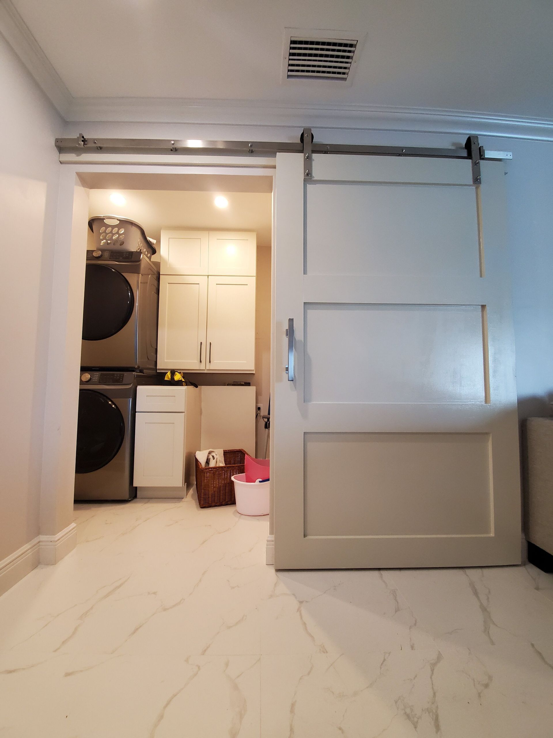 Laundry room with a sliding barn door. White appliances, cabinets, and flooring.