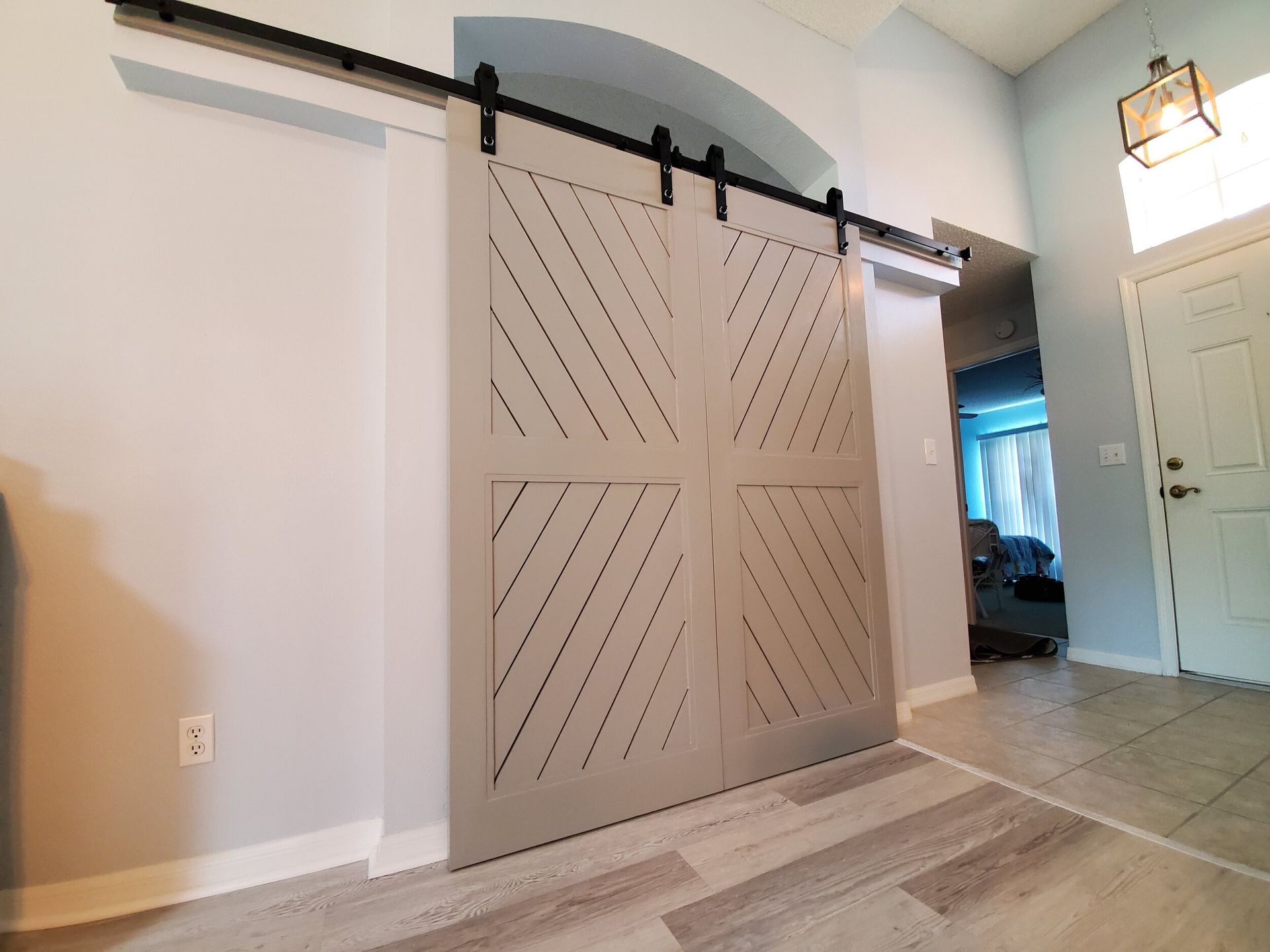 Gray barn door with diagonal cutouts, on a black sliding track, in a light-blue entry.