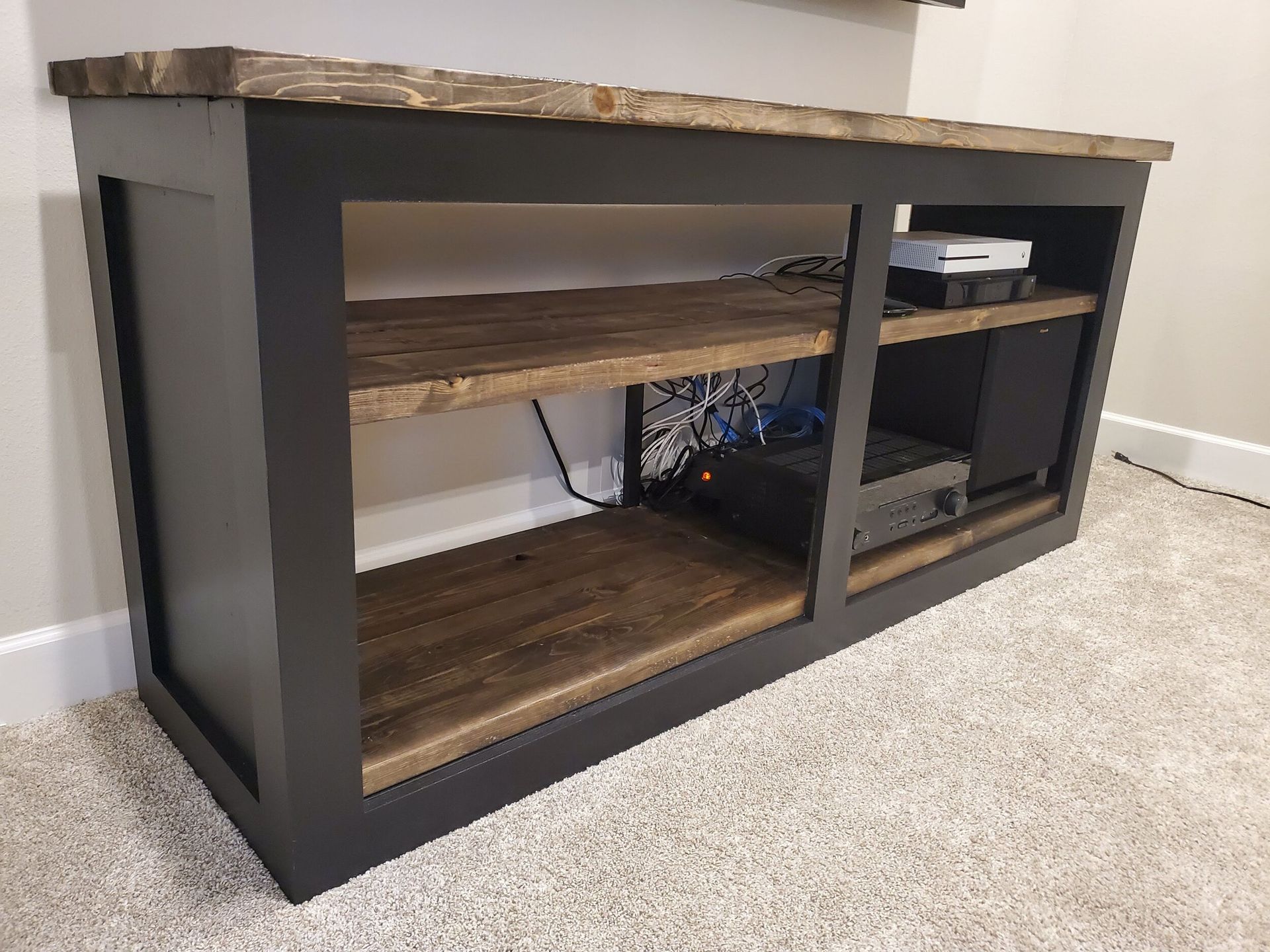 Dark-painted wooden entertainment console with open shelves, a dark top, and electronics visible.