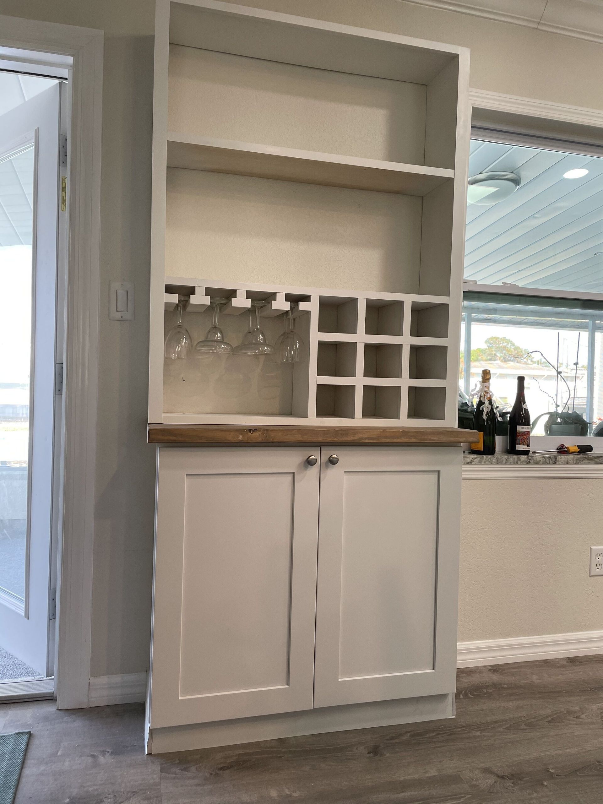 White built-in bar cabinet with open shelving, wine glass rack, wine cubbies, and cabinet doors.