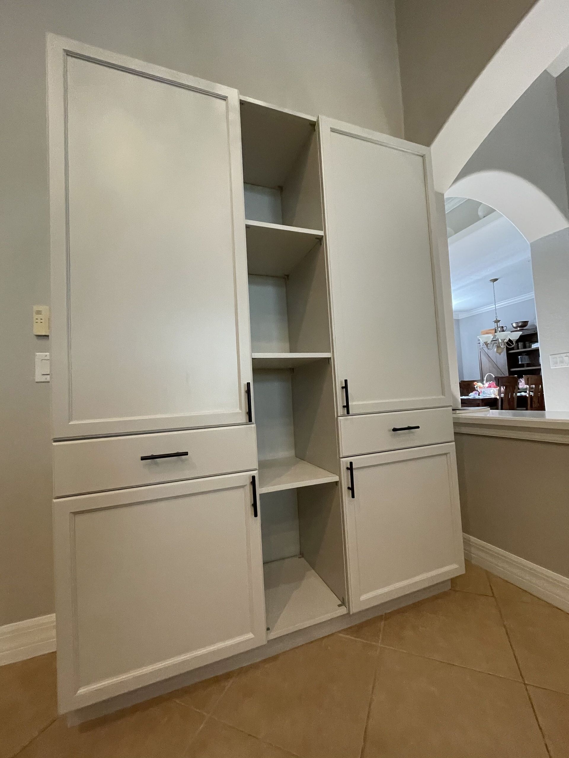 Tall white pantry cabinets with open center shelving in a home, with an arched doorway.