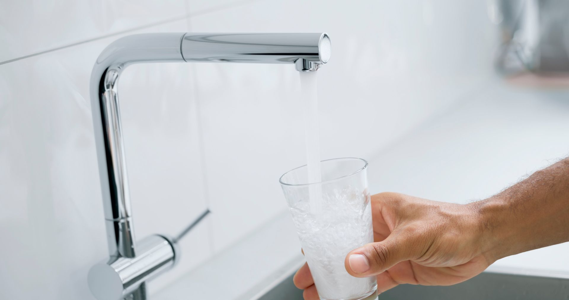 Man filling glass with clean water from residential water softening equipment system at home.