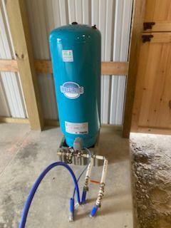 A blue water tank is sitting on top of a concrete floor next to a hose.