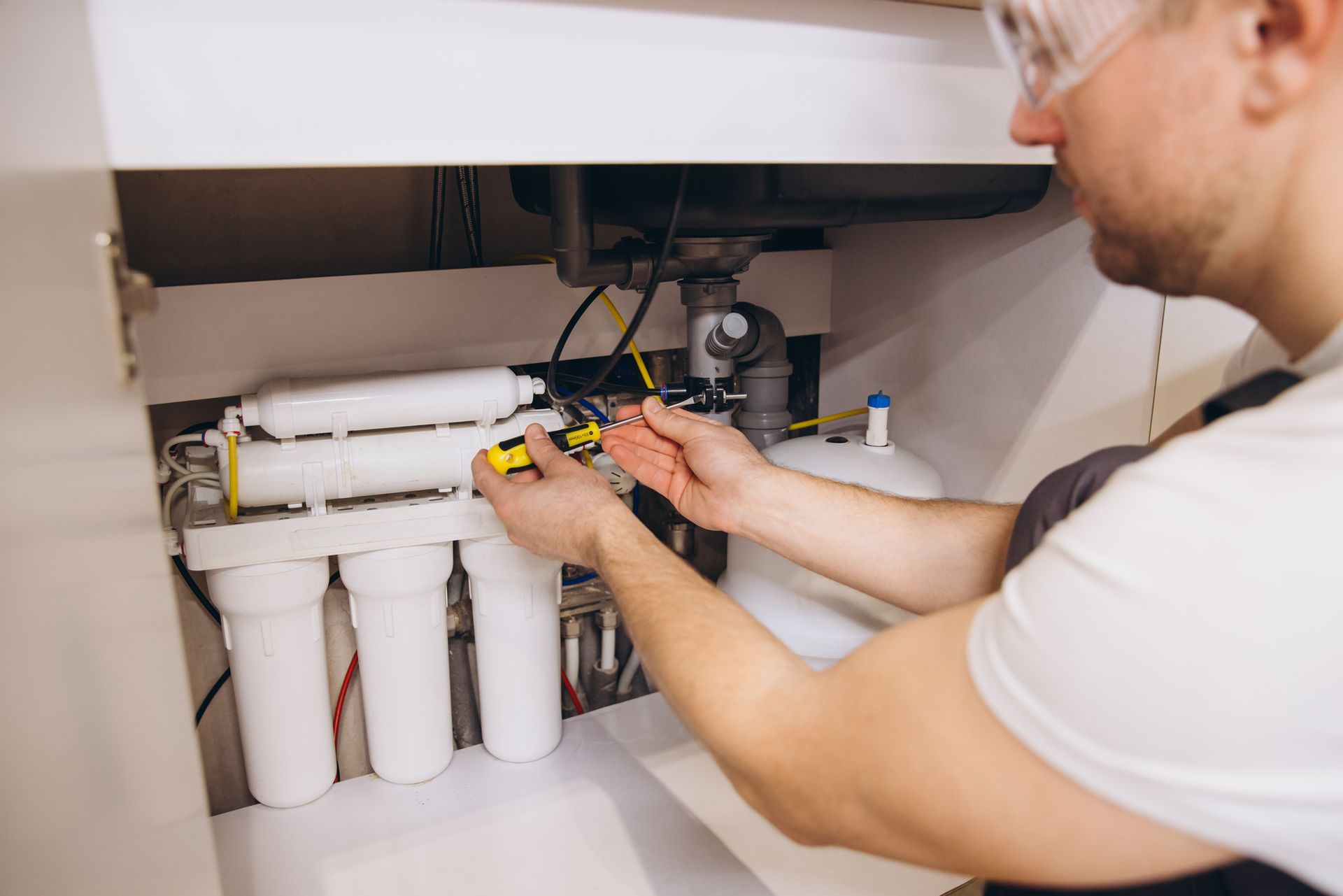 Plumber installing a water filter system under a kitchen sink.