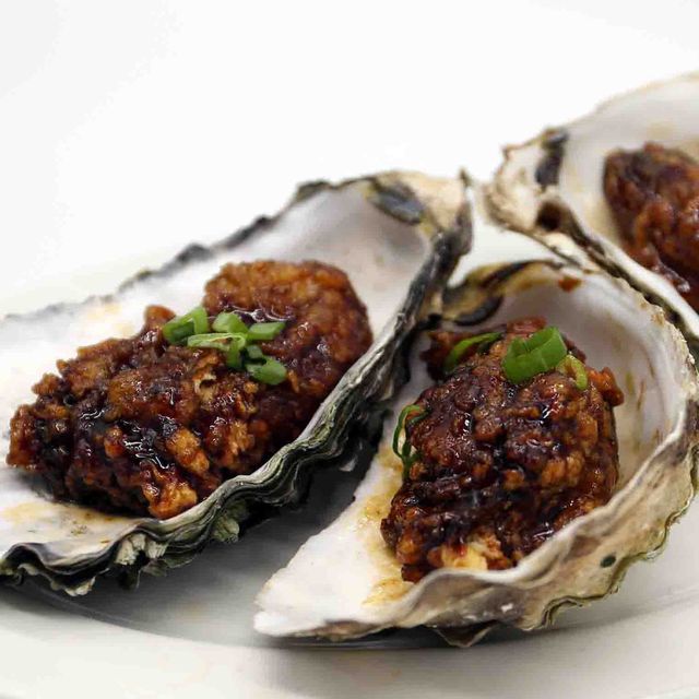 Grilled oysters topped with spicy minced meat and chopped green herbs on a white plate