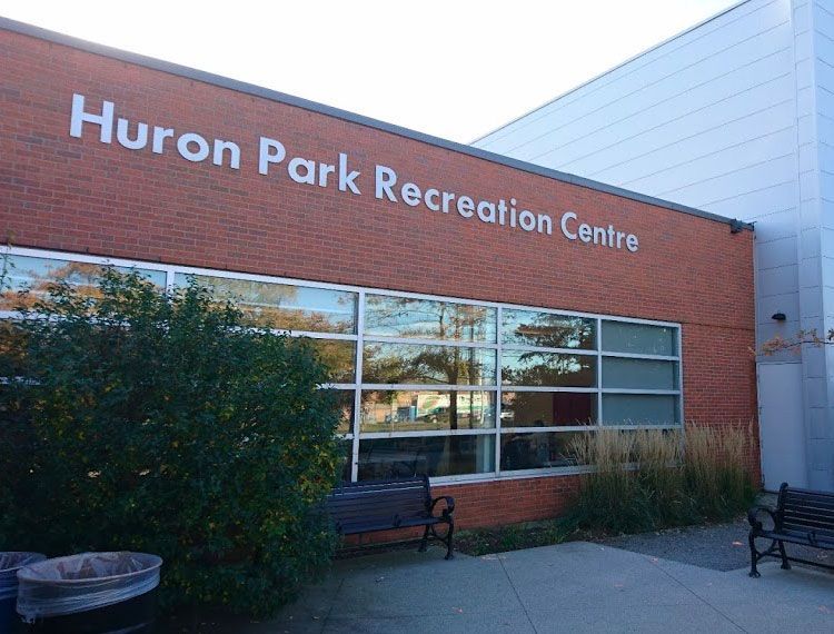 Huron Park Recreation Centre exterior. Red brick building with large windows and white sign, benches, and landscaping.
