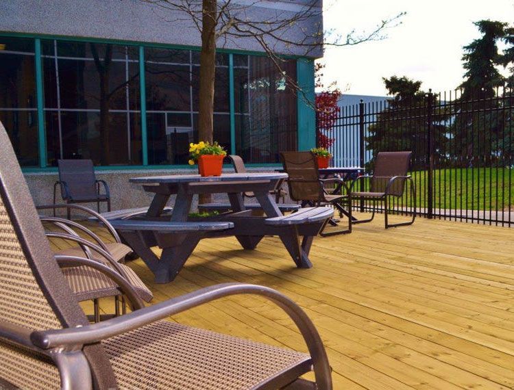 Wooden deck with picnic table and chairs, near a building and fence, flowers on the table.