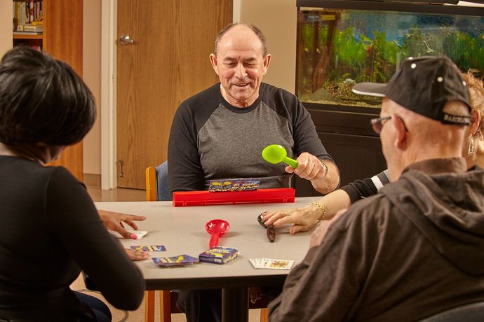 Group of people playing a card game at a table. One person holds a green mallet, smiling.