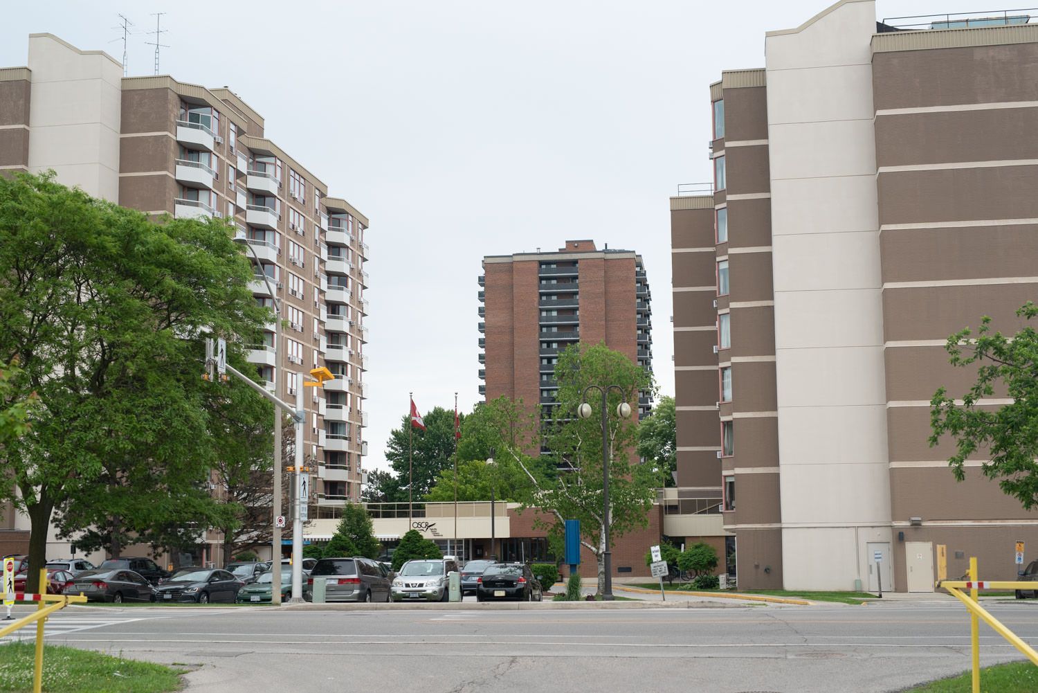 Three high-rise apartment buildings in a cloudy, urban setting; cars parked in front of buildings.