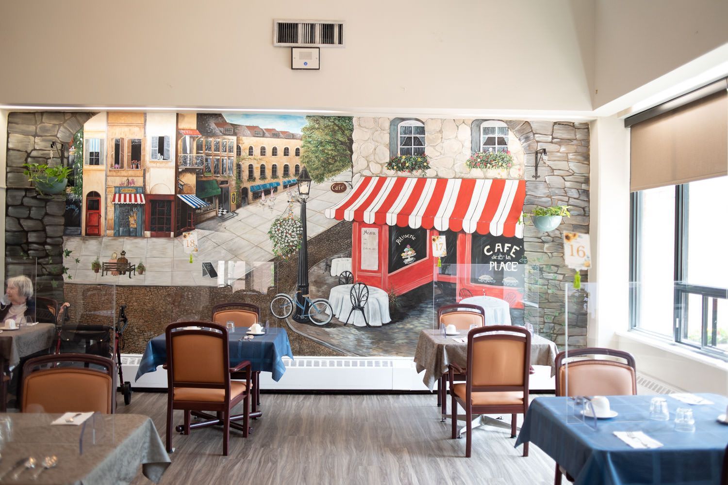 Dining room with mural of a European street scene; tables set with linens and chairs.
