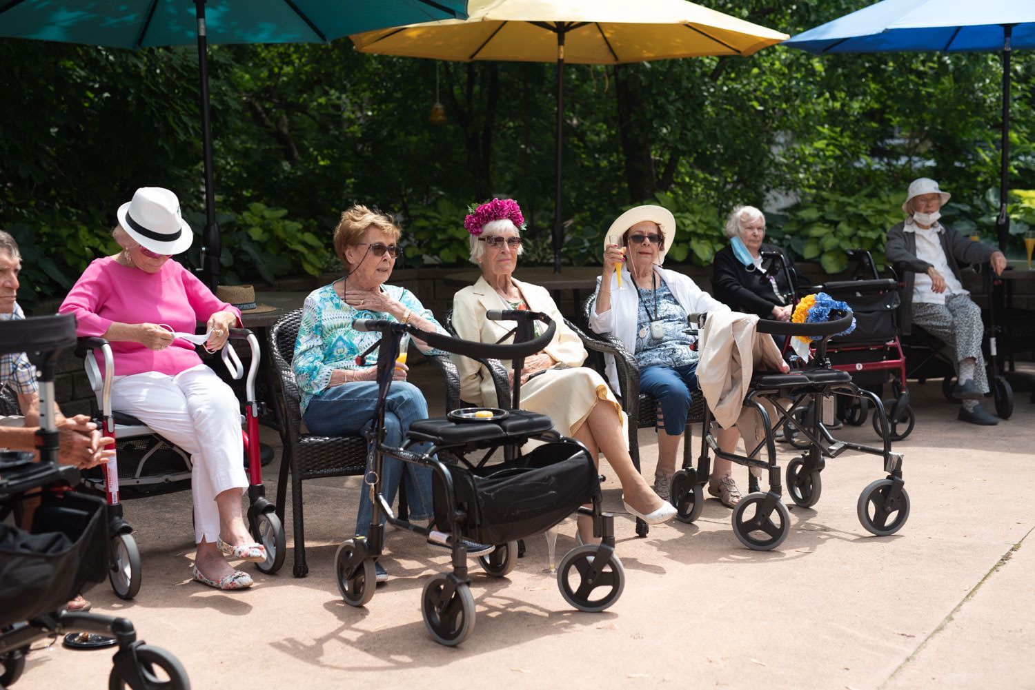 A group of people sitting outdoors under umbrellas, some using walkers.