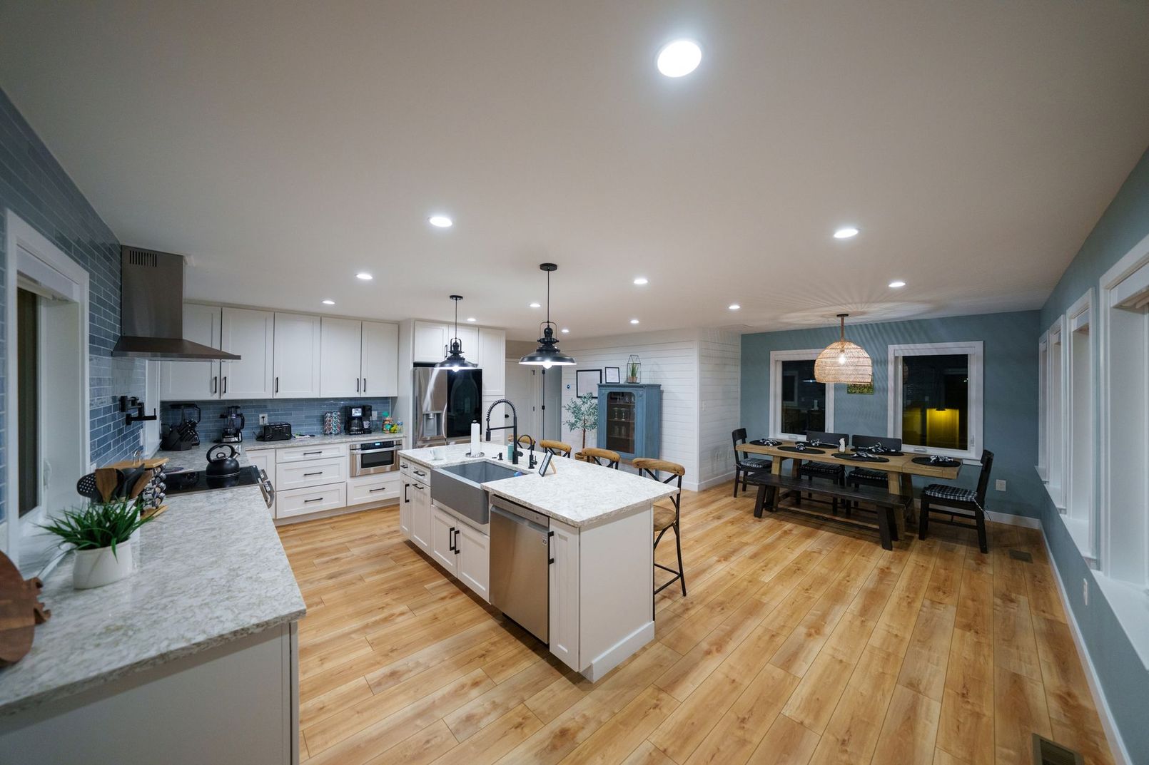 Spacious modern kitchen and dining area with white cabinets, island, wood floors, and pendant lights