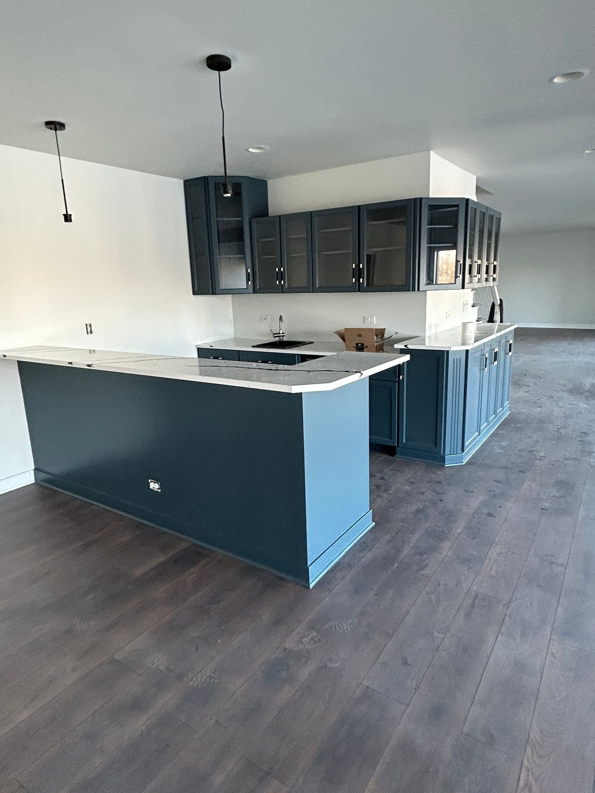 Empty modern kitchen with dark cabinets, white countertops, and dark wood floors