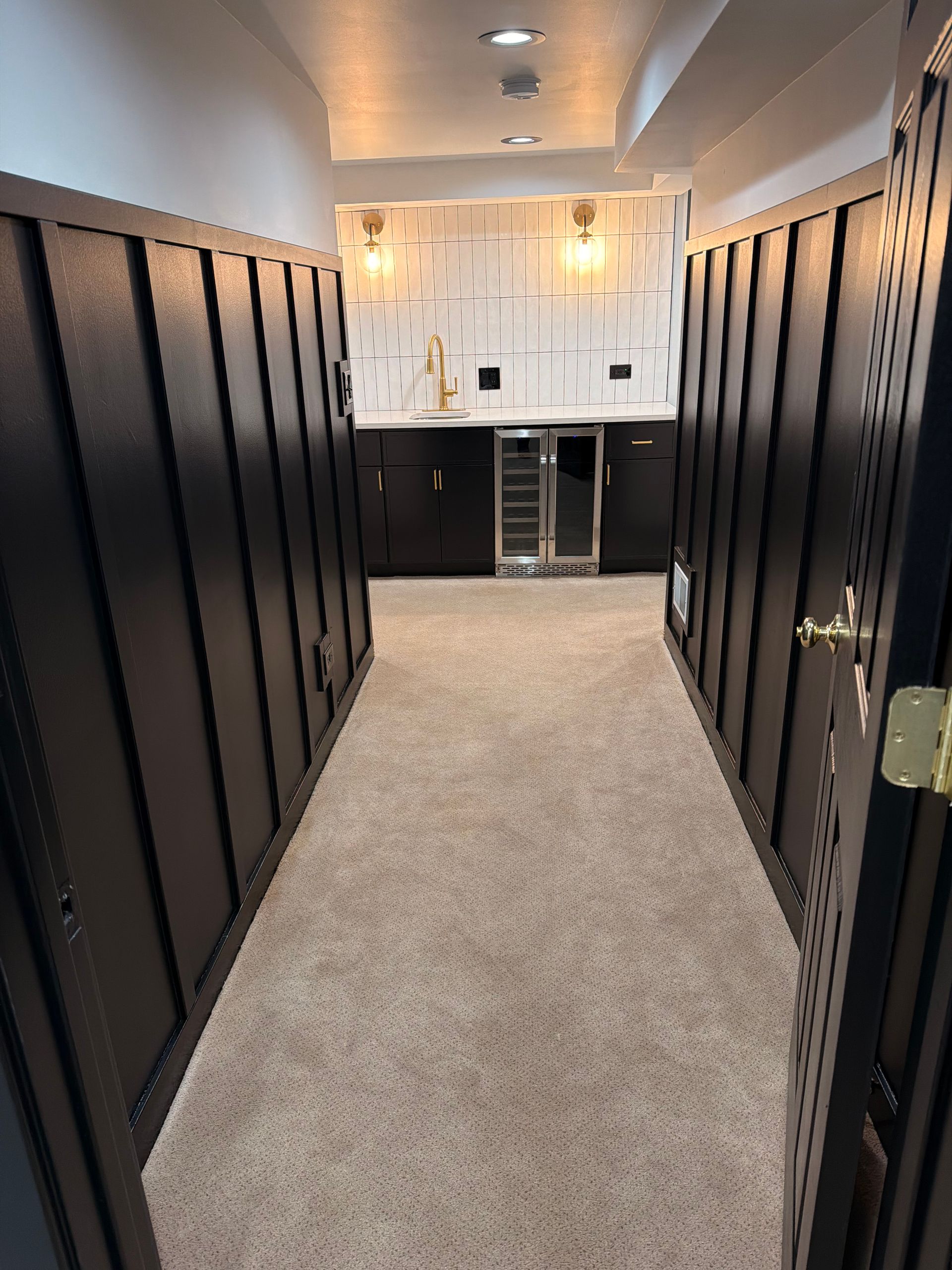 Narrow hallway with black lockers on both sides, carpeted floor, and a bright bathroom at the end.