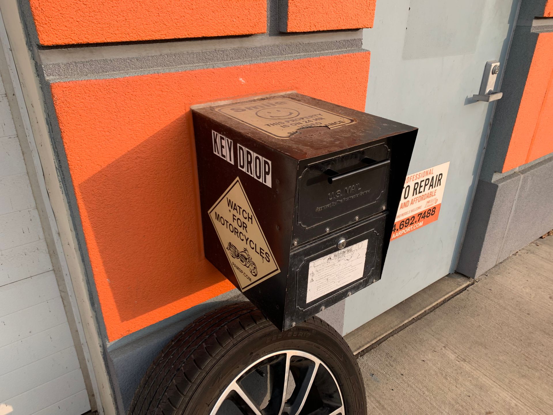 Black key drop box mounted on orange wall, over a car tire. | Absolute Auto Repairs & Sales