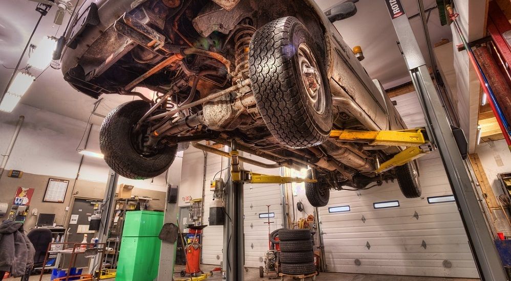 Car raised on a lift in a garage, view from below, showing undercarriage, tires, and lift equipment. | Absolute Auto Repairs & Sales