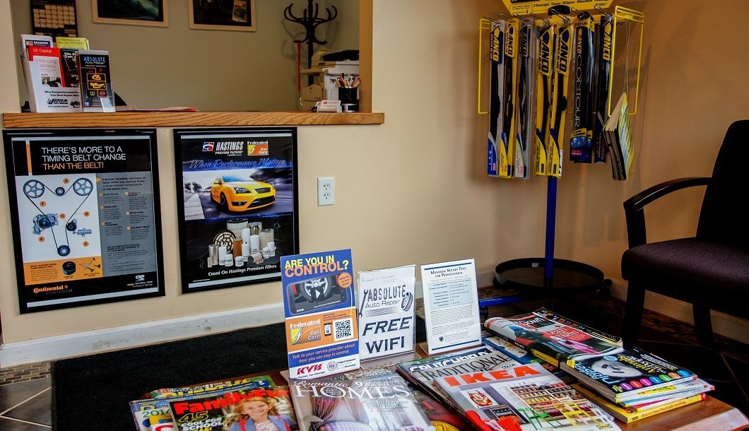 Waiting area with magazines, posters, display rack of yellow items, and a dark chair. | Absolute Auto Repairs & Sales