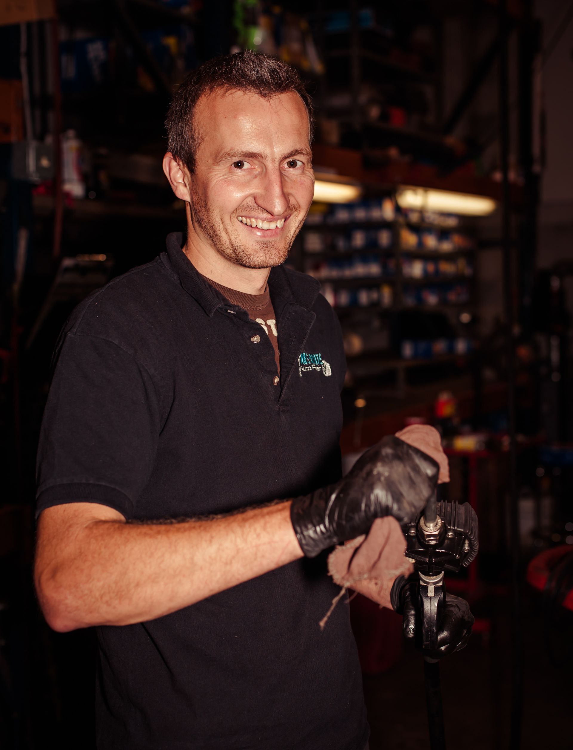 Man in black polo shirt and gloves, smiling while working on machinery in a shop. | Absolute Auto Repairs & Sales