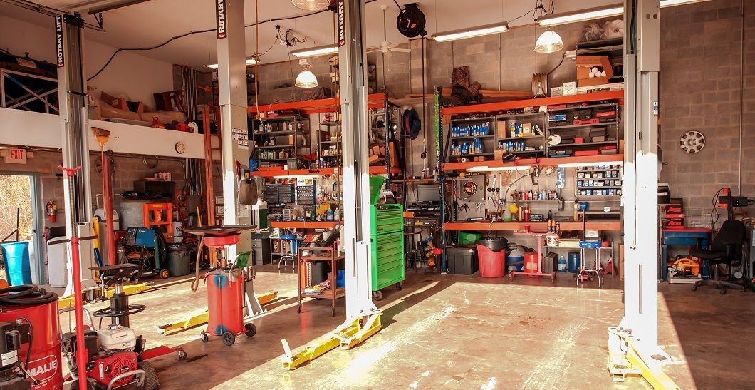 A car repair shop interior with vehicle lift, tools, and shelves filled with equipment. | Absolute Auto Repairs & Sales