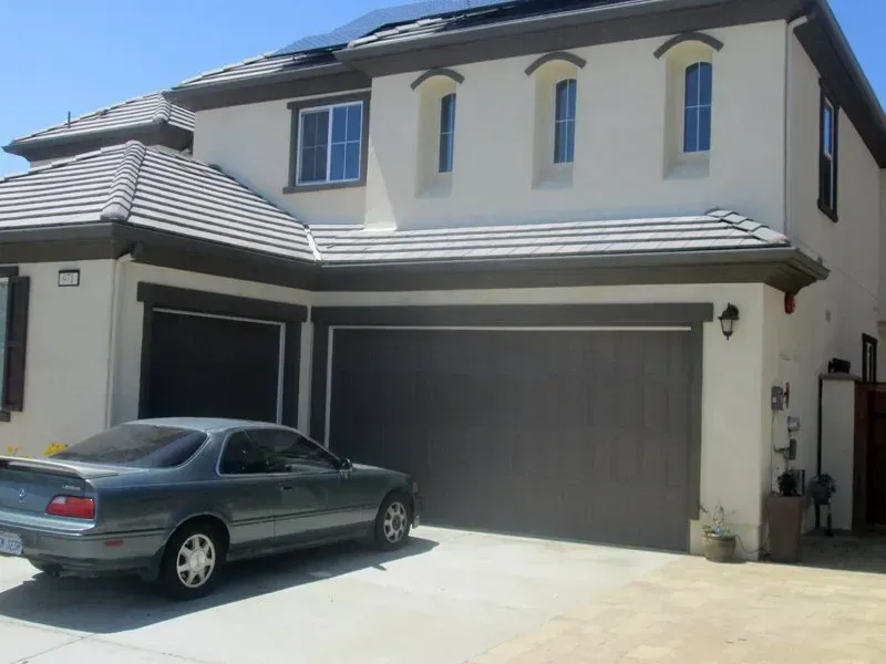 Two-story beige house with a gray garage and a car parked in the driveway