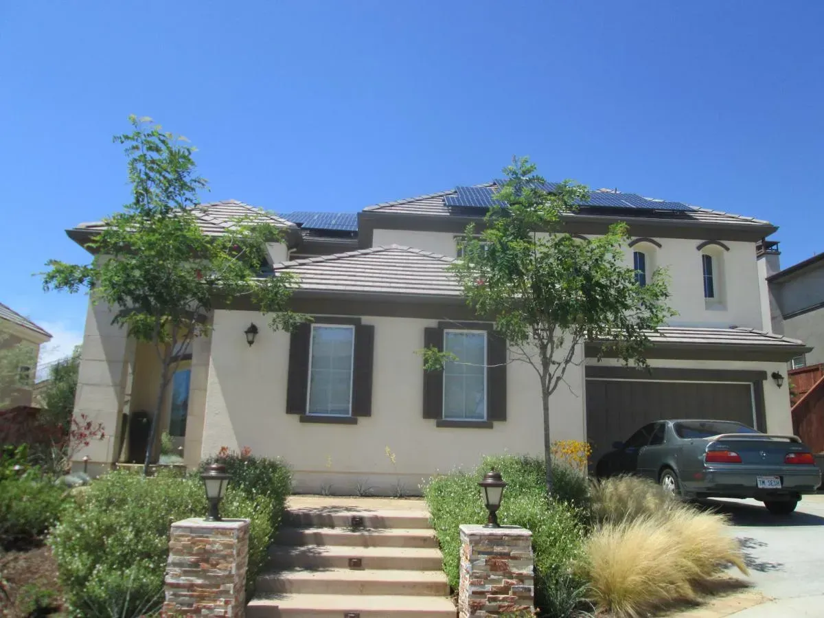 Two-story beige house with front steps, trimmed shrubs, and a car parked in the driveway