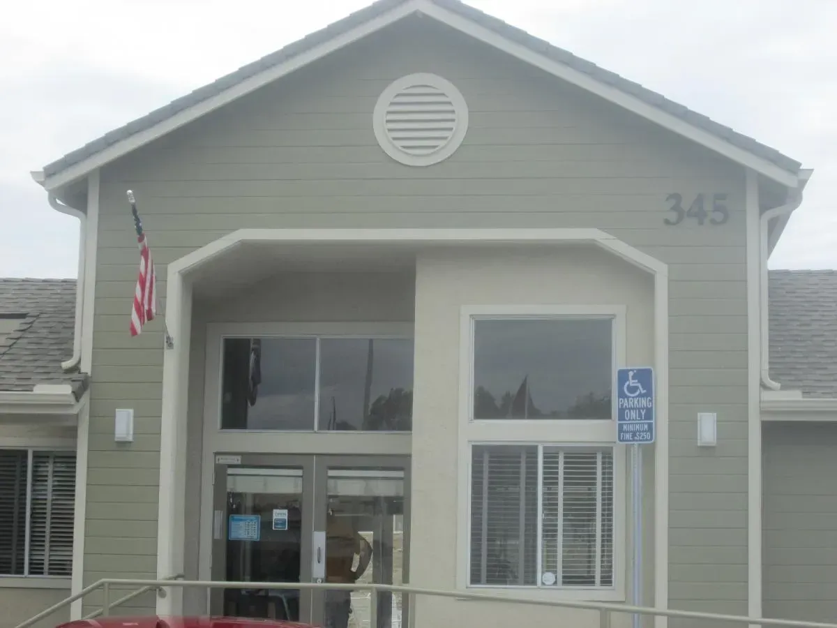 Front entrance of a gray building with an American flag, handicap sign, and the number 345 above the door.