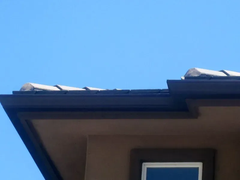 House roofline against a clear blue sky with a small window below the eaves